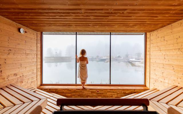 Frau am Panoramafenster in der Sauna genießt den Ausblick auf den Schwimmteich