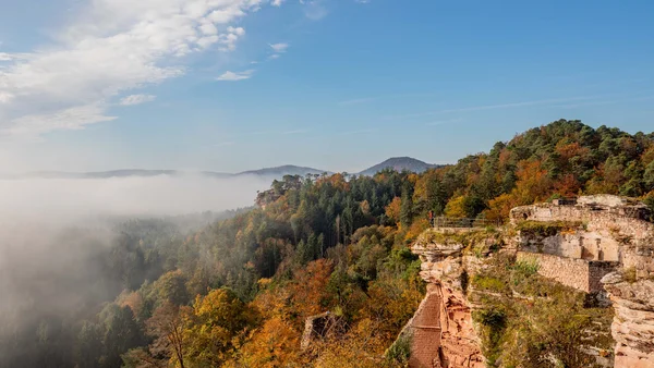 Felsenburg in herbstlichem Wald mit Nebel und blauem Himmel