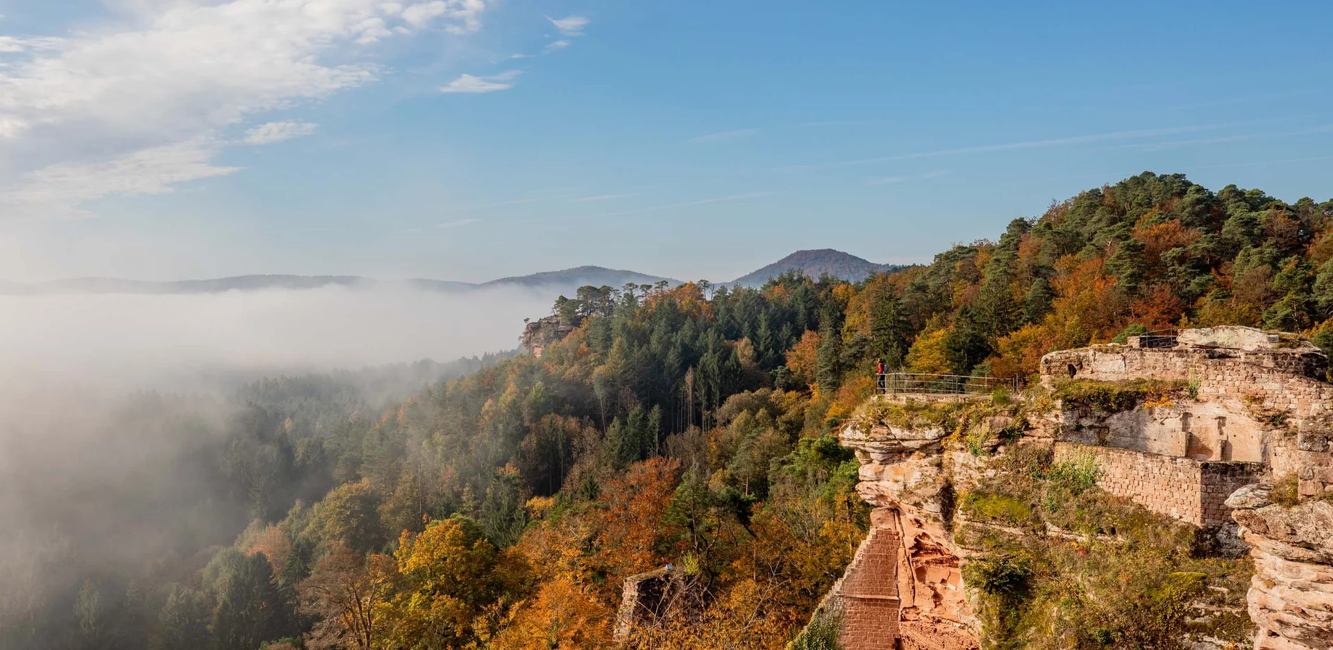 Felsenburg in herbstlichem Wald mit Nebel und blauem Himmel