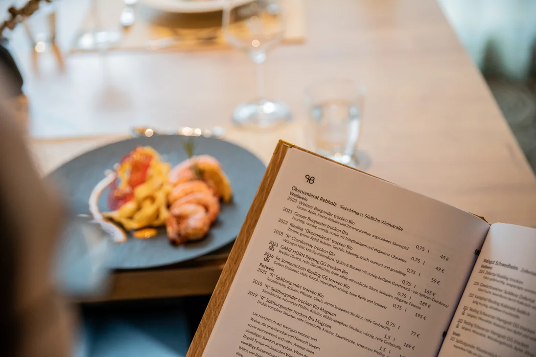 Person hält eine Wein- und Speisekarte in einem Restaurant mit einem Teller im Hintergrund