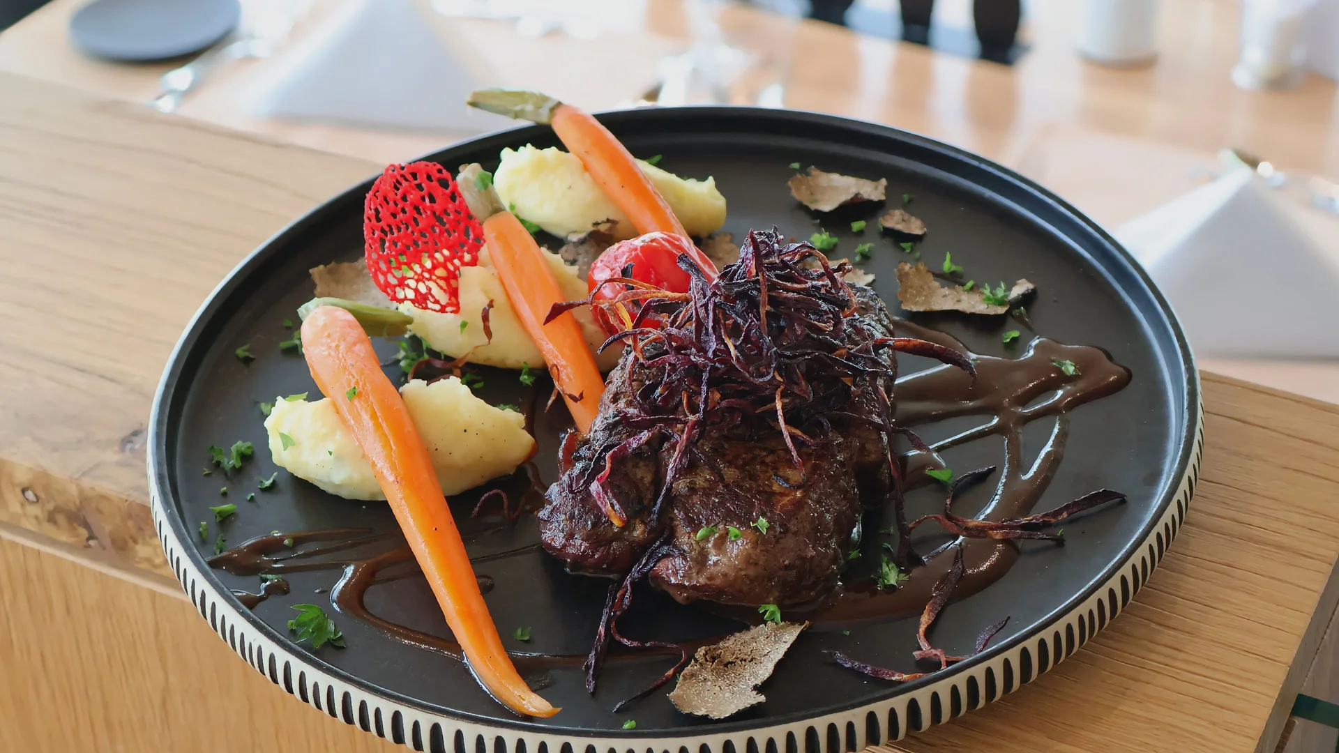 Gebratenes Fleisch mit Karotten, Kartoffelpüree und dunkler Sauce auf einem schwarzen Teller