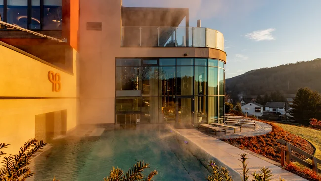 Dampfender Außenpool neben modernem Gebäude bei Sonnenuntergang