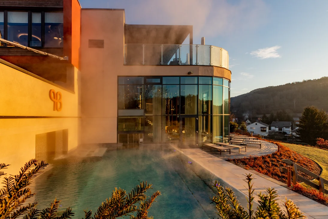 Dampfender Außenpool neben modernem Gebäude bei Sonnenuntergang