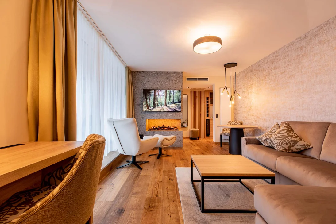 Wohnzimmer mit Kamin, Fernseher, Sesseln und Sofa in warmem Design