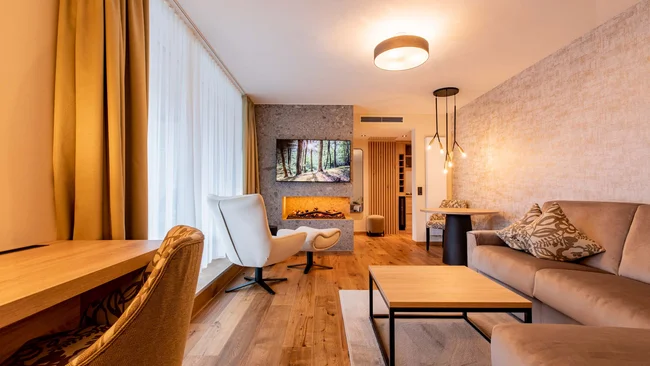 Wohnzimmer mit Kamin, Fernseher, Sesseln und Sofa in warmem Design