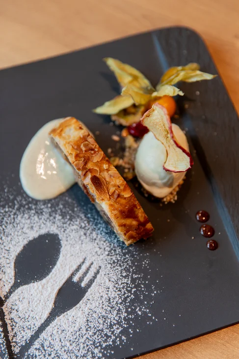 Dessert mit Mandelkuchen, Vanillesoße und dekorativen Früchten auf schwarzem Teller