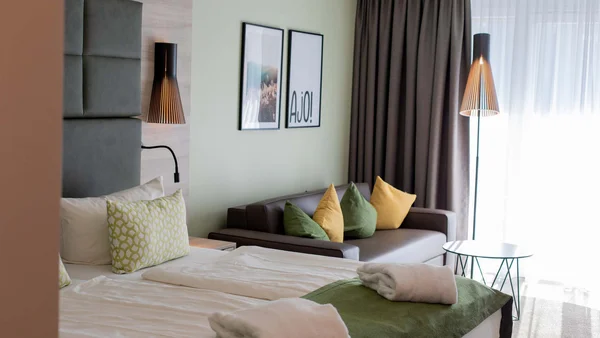 Modernes Hotelzimmer mit Doppelbett, Sofa, Kissen und Stehlampe