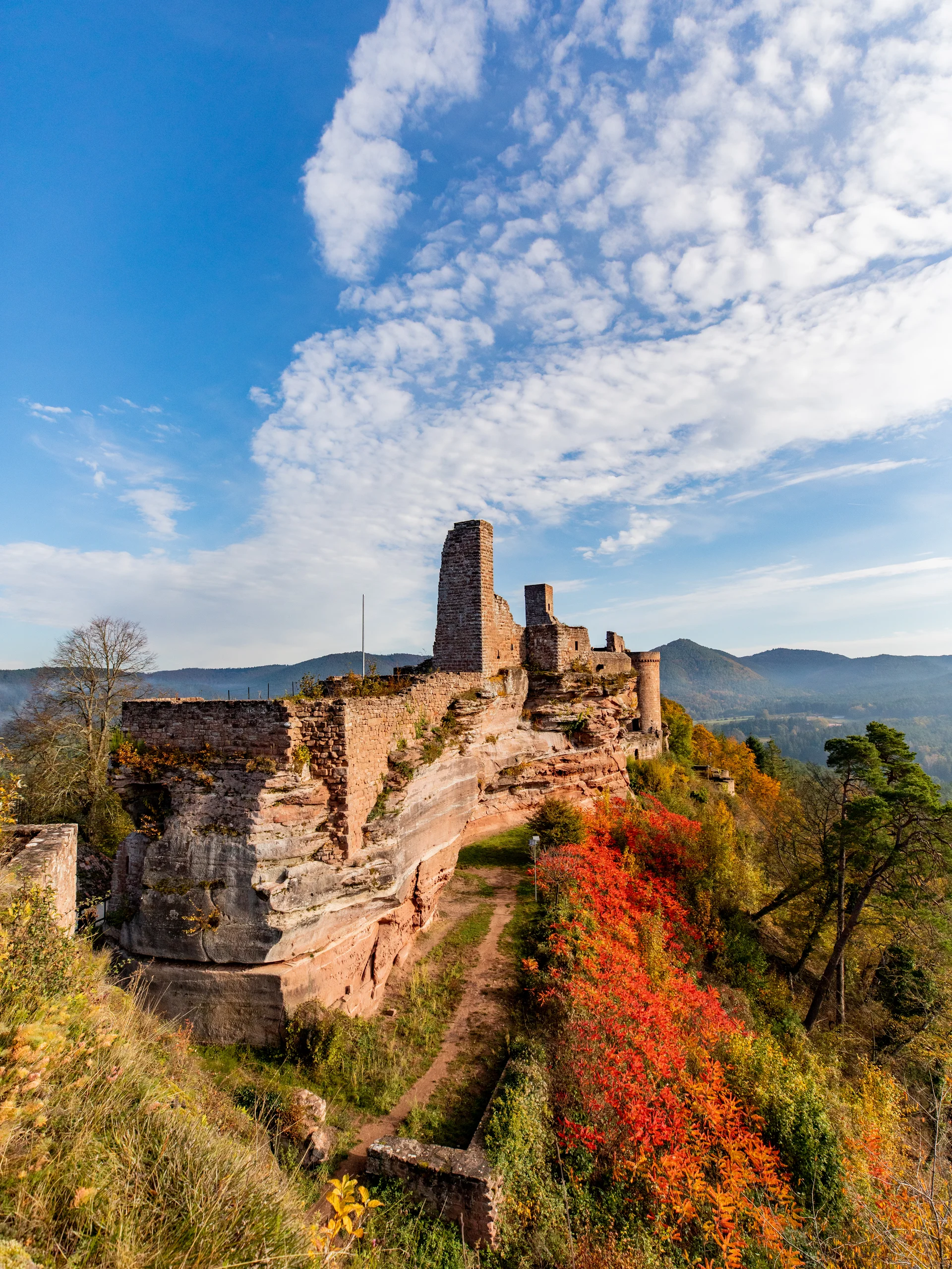 Ruine einer Burg auf einem Hügel mit Herbstlaub und blauem Himmel
