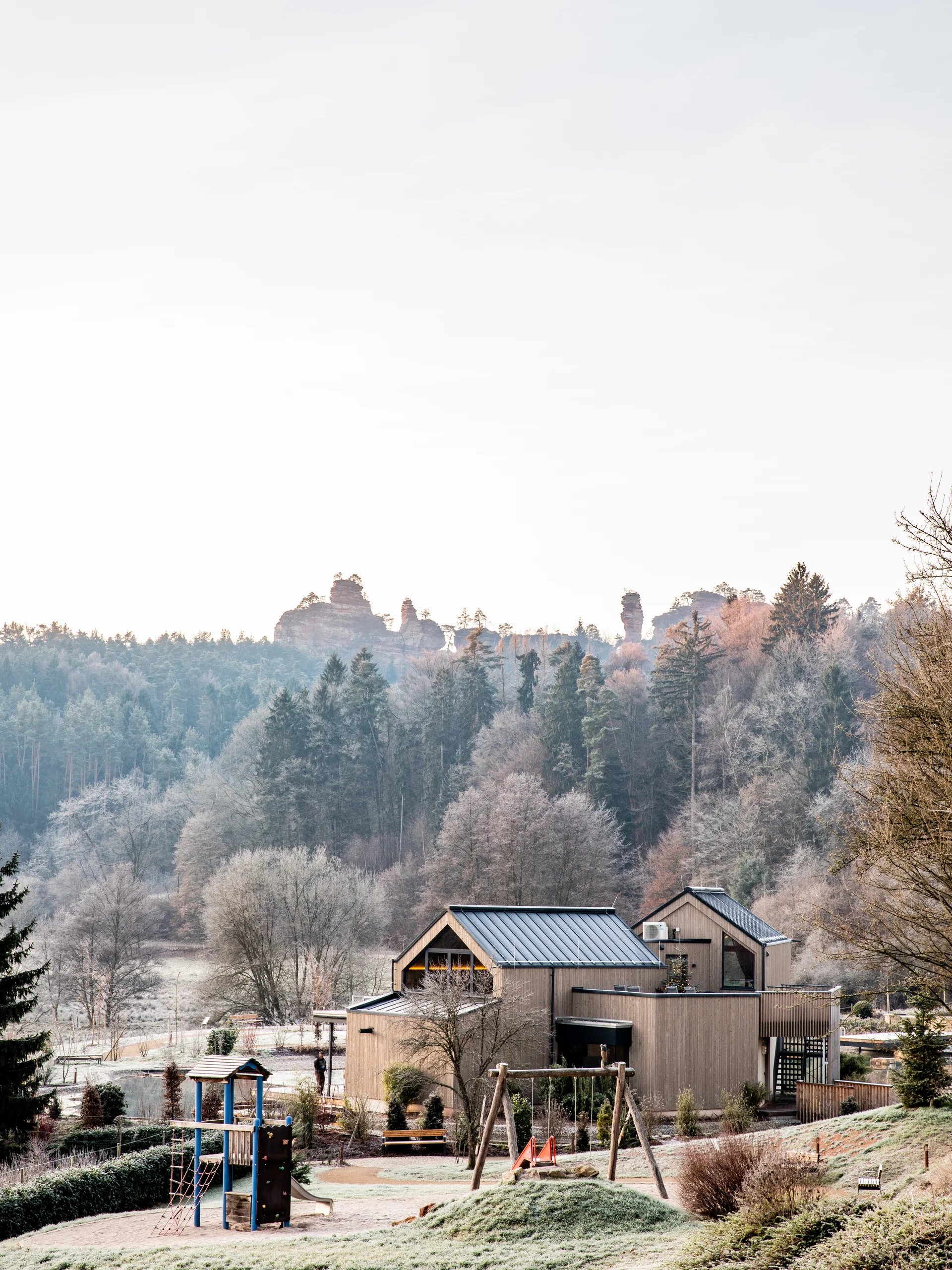 Spielplatz und modernes Haus vor bewaldeten Hügeln im frostigen Morgenlicht