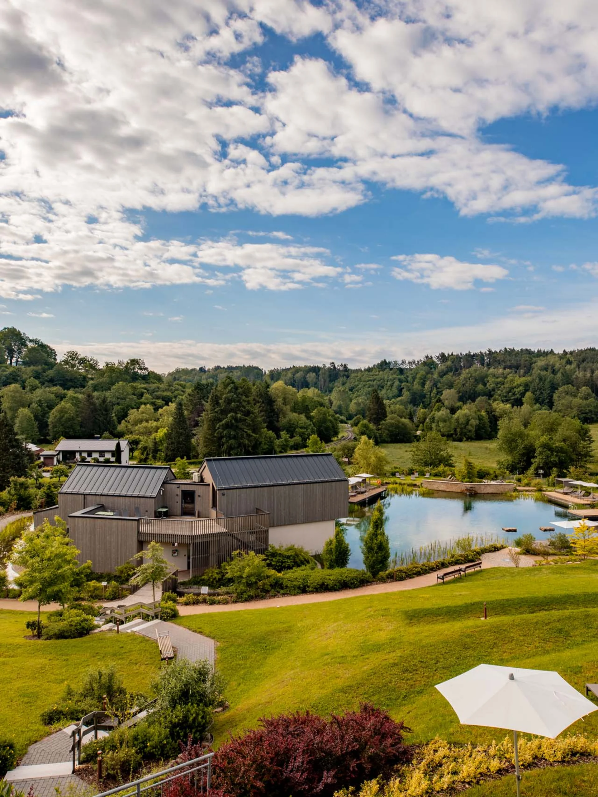 Landschaft mit modernem Haus, Teich, grünen Hügeln und bewölktem Himmel