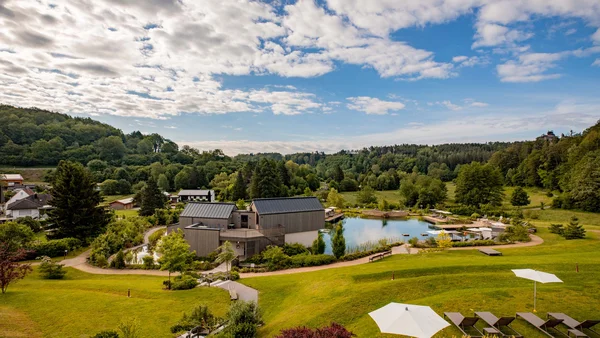 Landschaft mit modernem Haus, Teich, grünen Hügeln und bewölktem Himmel