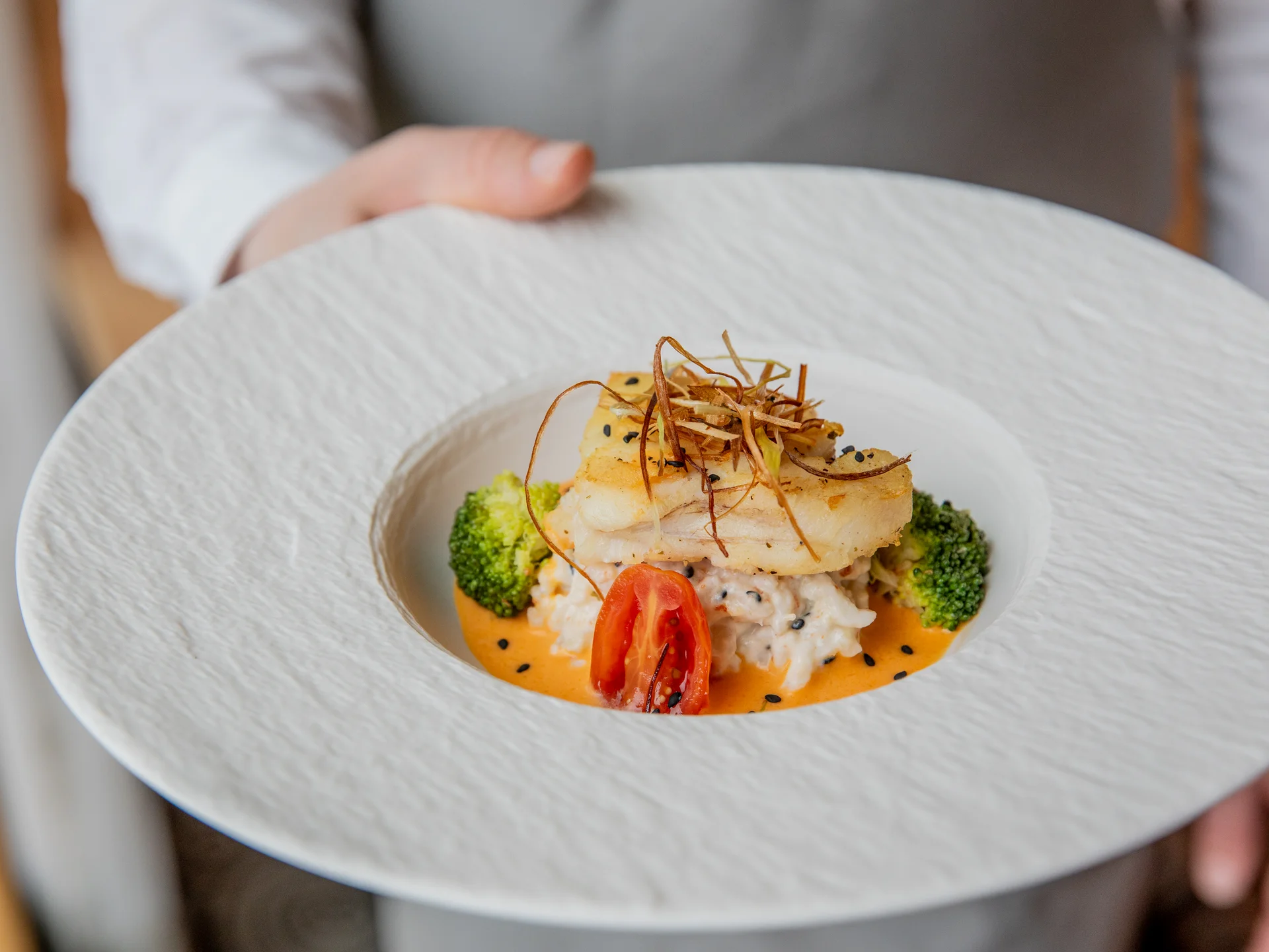 Elegantes Fischgericht mit Reis, Tomate, Brokkoli und Garnitur auf weißem Teller