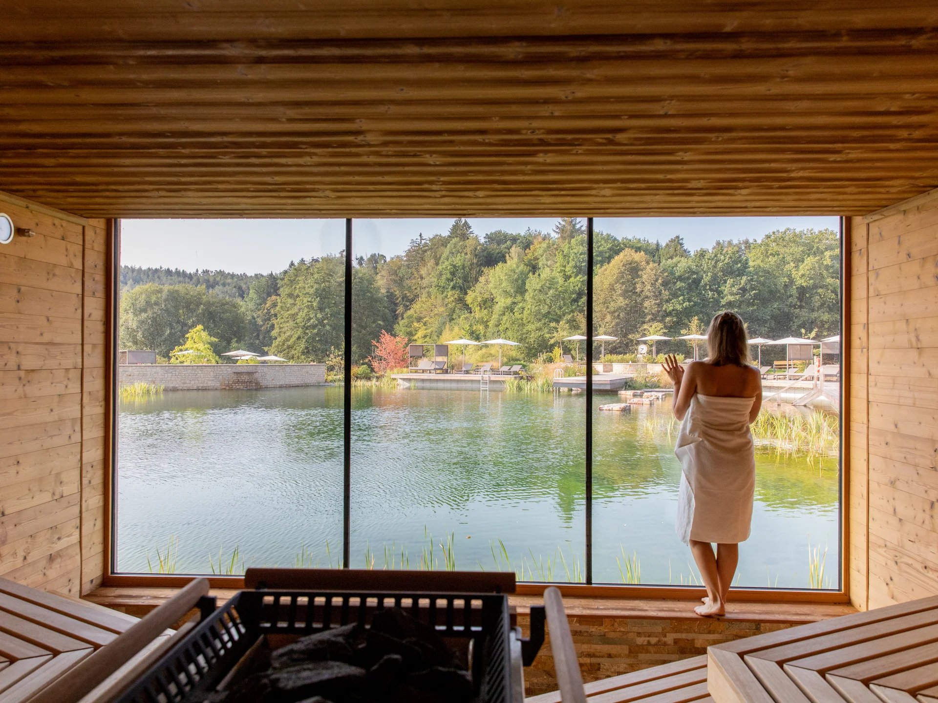 Frau in Sauna mit Blick auf See und Wald durch großes Panoramafenster