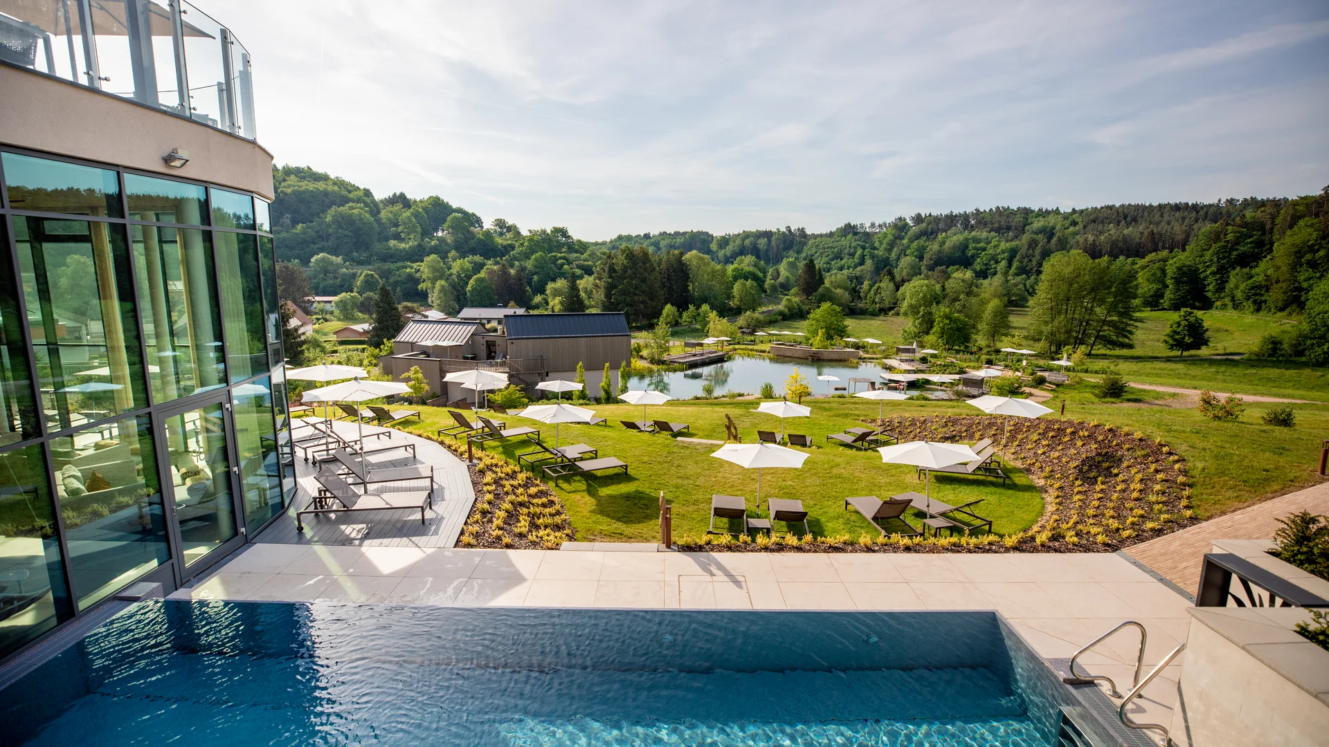Pressebilder Poolbereich mit Liegestühlen, Sonnenschirmen und Blick auf Wald und Wiese