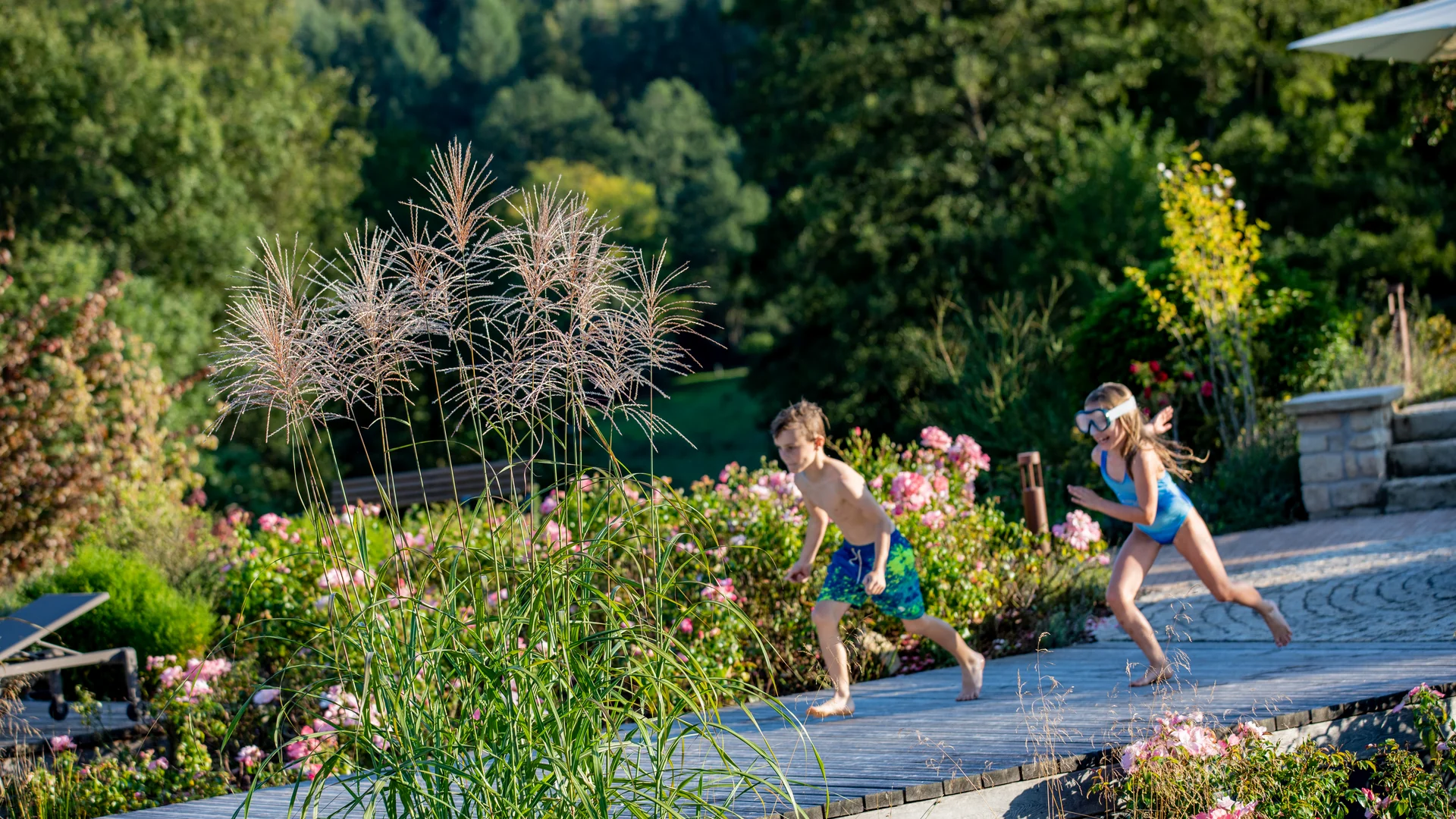Zwei Kinder laufen barfuß auf Terrasse im Garten mit Blumen und Bäumen