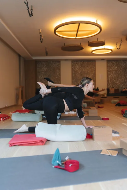 Frau in Yoga-Studio macht Dehnübung auf Matte mit Kissen und Blöcken
