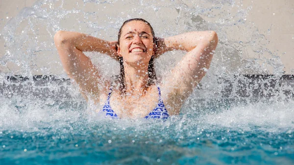 Frau genießt Wasser in Schwimmbad mit Händen hinter dem Kopf