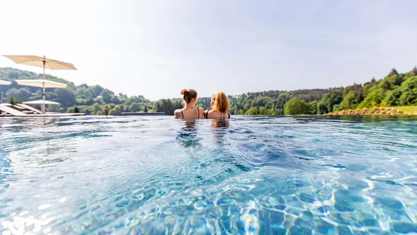Zwei Frauen im Pool mit Blick auf bewaldete Hügel