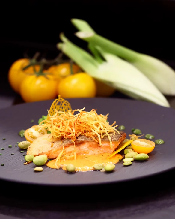 Gourmetgericht mit gebratenem Fisch, Sauce und Gemüse auf schwarzem Teller