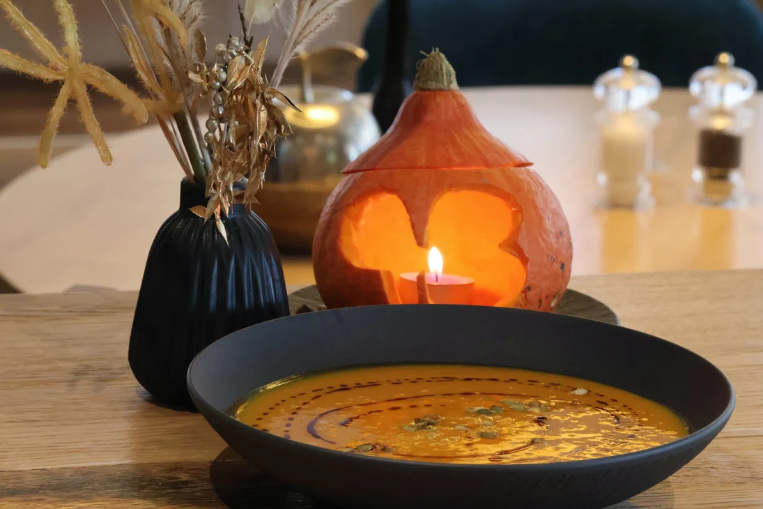 Kürbissuppe in schwarzer Schale mit Kürbis-Laterne und getrockneten Blumen