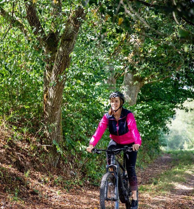 Frau fährt Mountainbike auf Waldweg unter grünen Bäumen