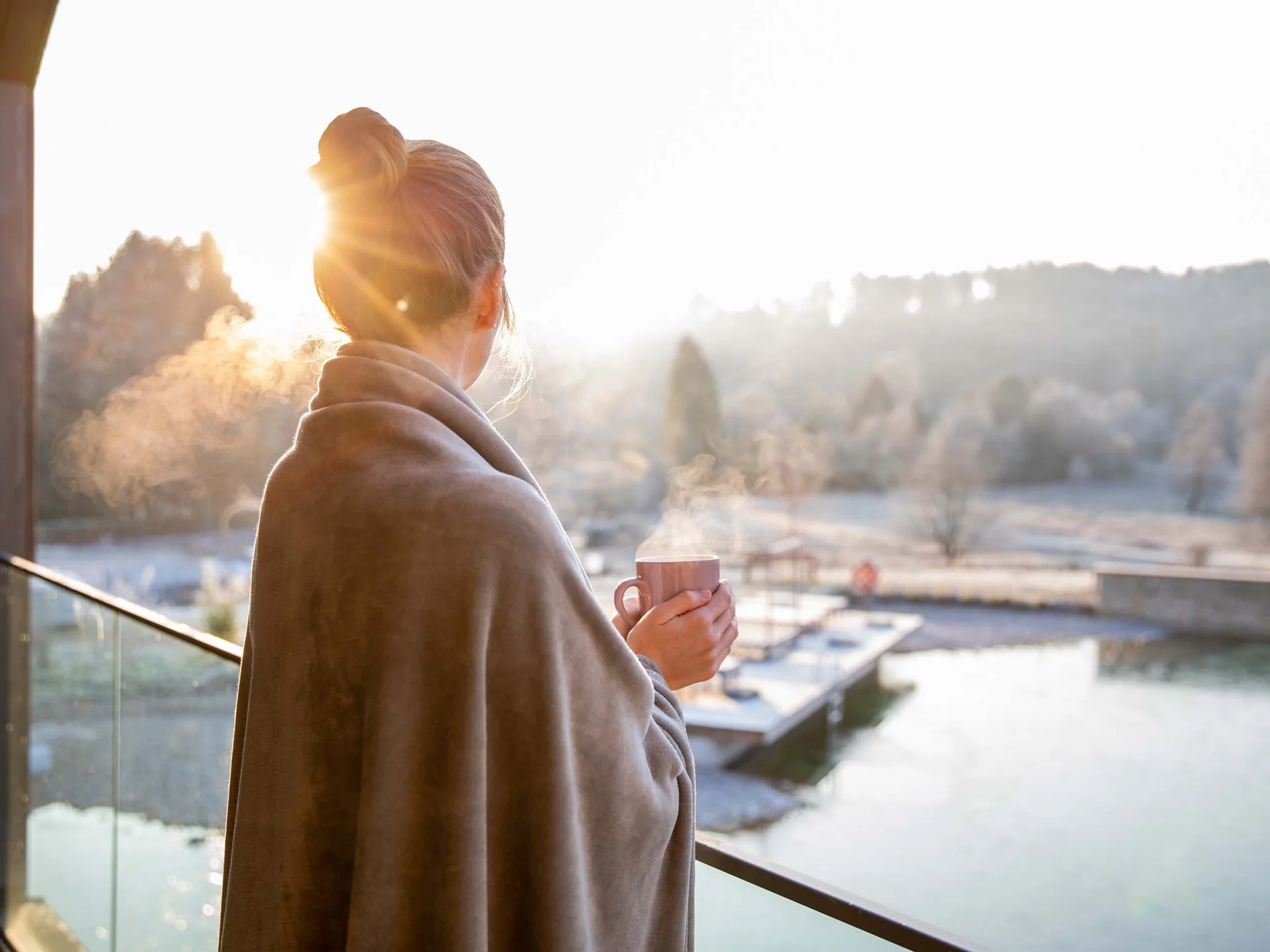 Dampf, Duft, Dahn: Sauna-Erlebnis mit Naturblick Frau mit Decke trinkt heißen Tee auf Balkon bei Sonnenaufgang im Winter