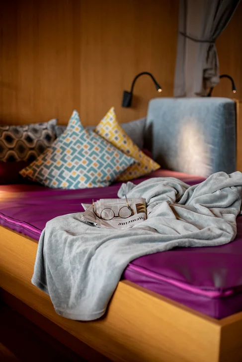 Vapeur, senteur, bonheur : sauna sensorielavec vue naturelle Coin salon confortable avec coussins colorés, journal et lunettes sur coussin violet