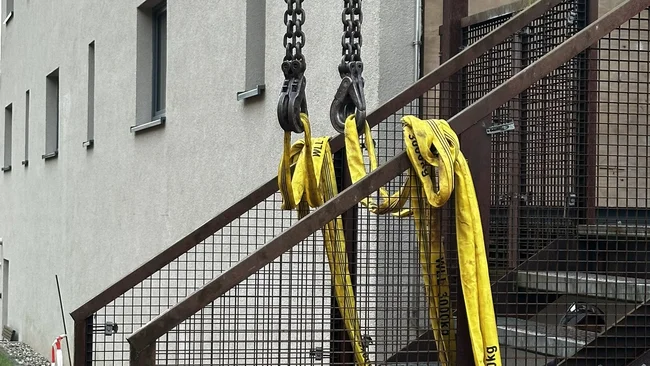 Élingues jaunes et chaînes fixées à un escalier métallique, avec un ouvrier partiellement visible
