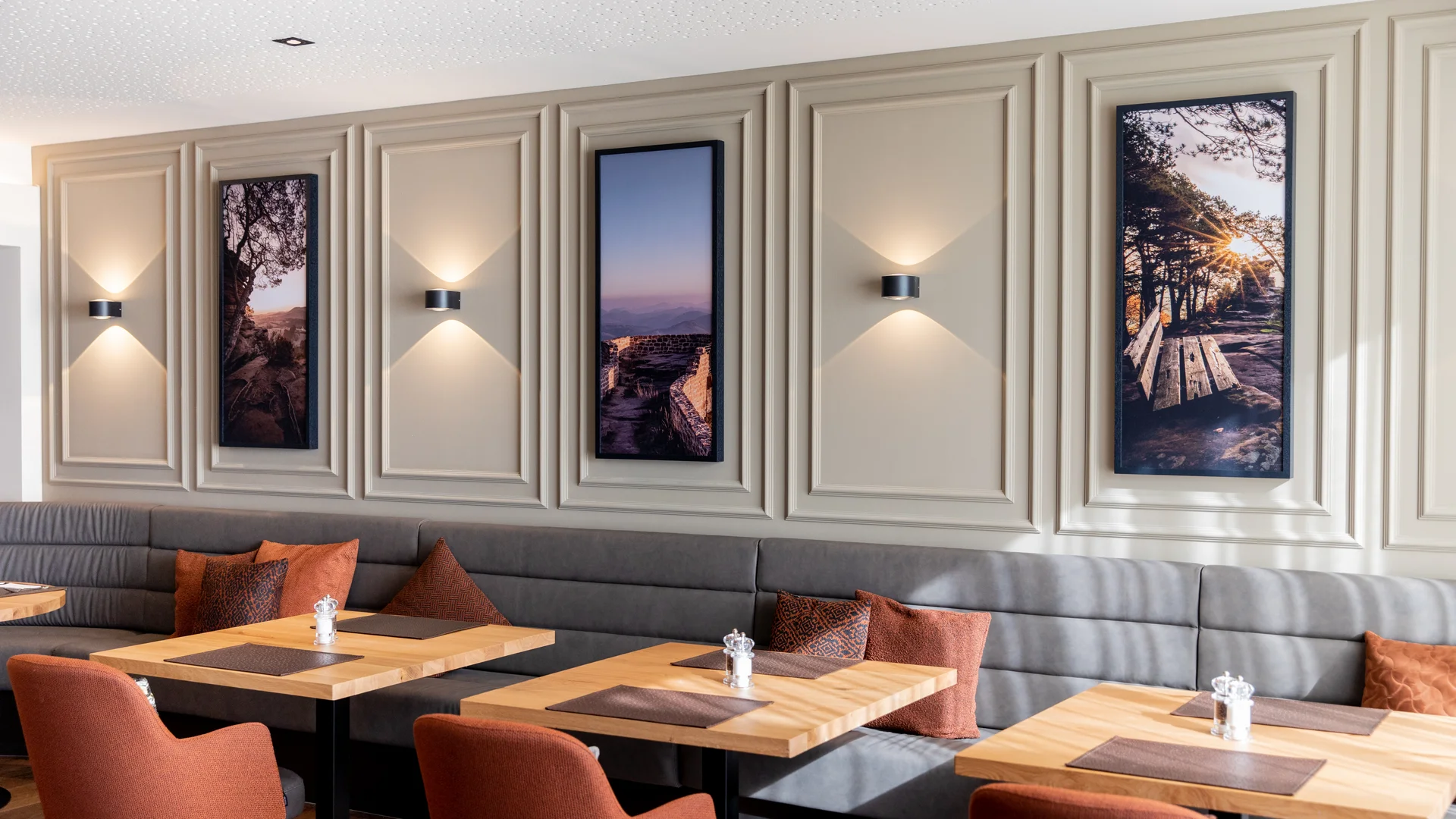Pressebilder Modernes Restaurant mit grauen Sitzbänken, orangen Stühlen und Naturbildern an der Wand