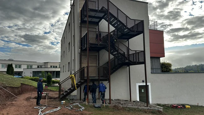 Des ouvriers installent un escalier extérieur noir sur un bâtiment à plusieurs étages