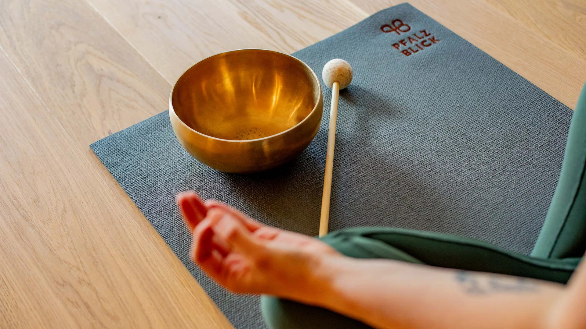 Person sitzt meditierend mit Klangschale und Schlägel auf Yogamatte