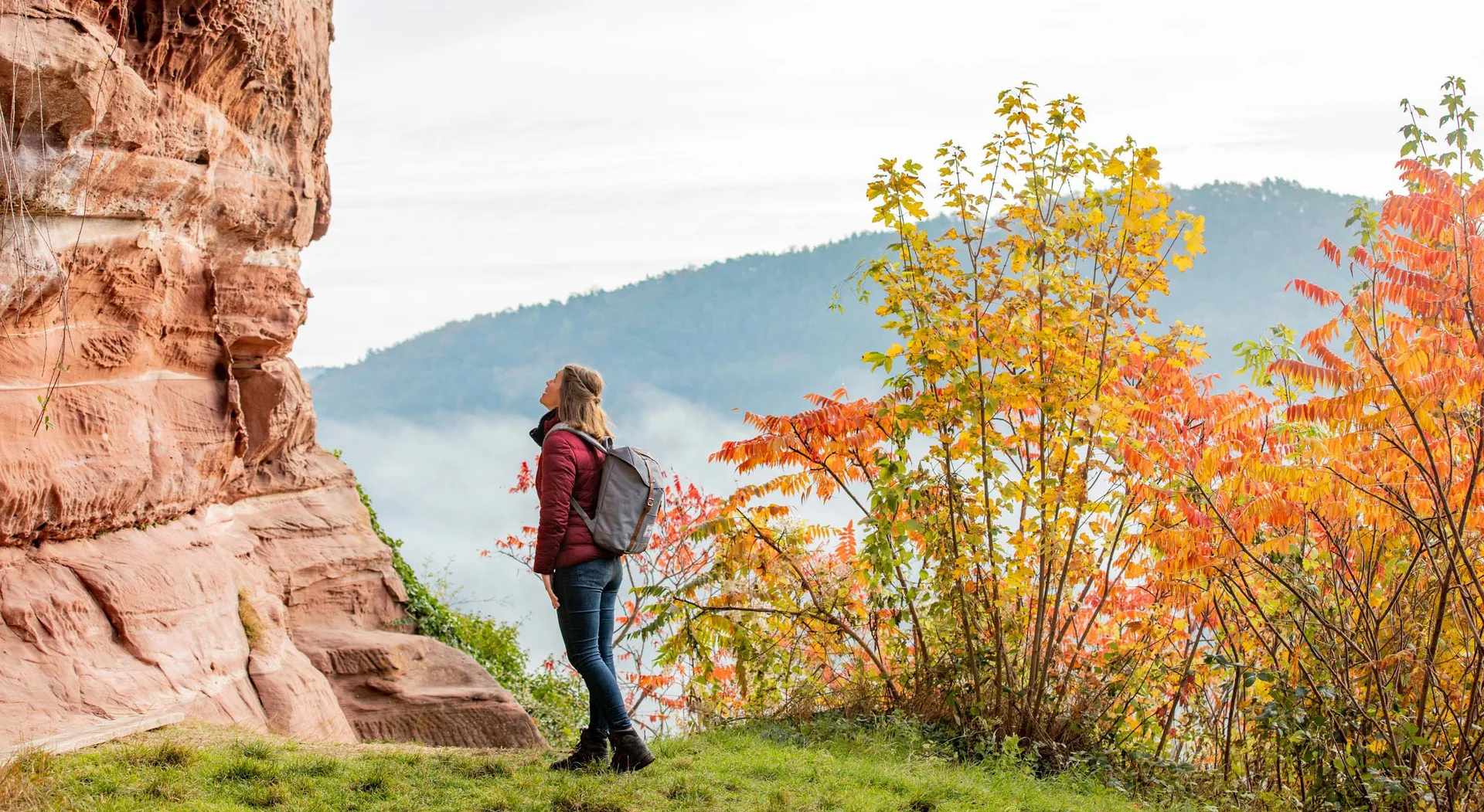 Frau mit Rucksack betrachtet roten Felsen im herbstlichen Wald