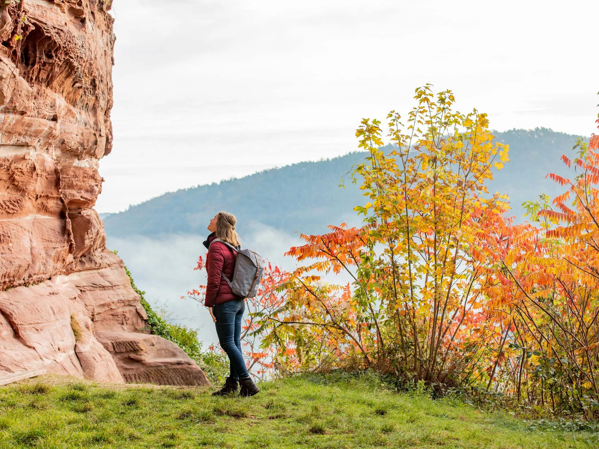 Frau mit Rucksack betrachtet roten Felsen im herbstlichen Wald