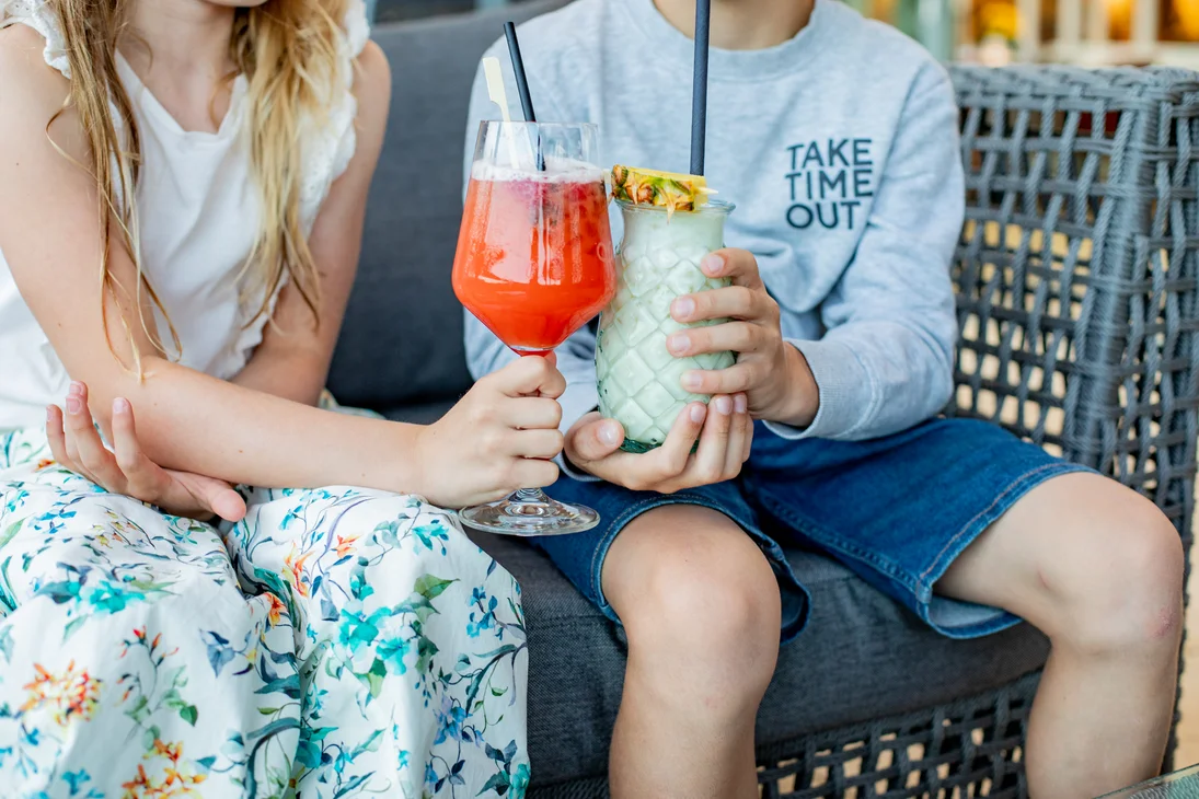 Zwei Kinder halten bunte Getränke in Gläsern und sitzen zusammen