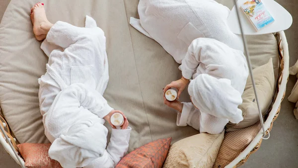 Zwei Personen in Bademänteln trinken Kaffee und entspannen auf einem Sofa