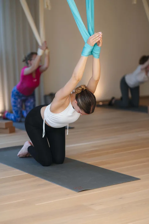 Frau macht Aerial Yoga Pose auf Yogamatte in hellem Studio