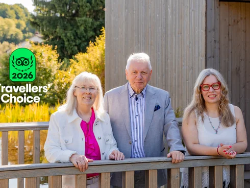 Blog – Actualités du Pfalzblick Wald Spa Resort Trois adultes souriants devant un bâtiment en bois par une journée ensoleillée