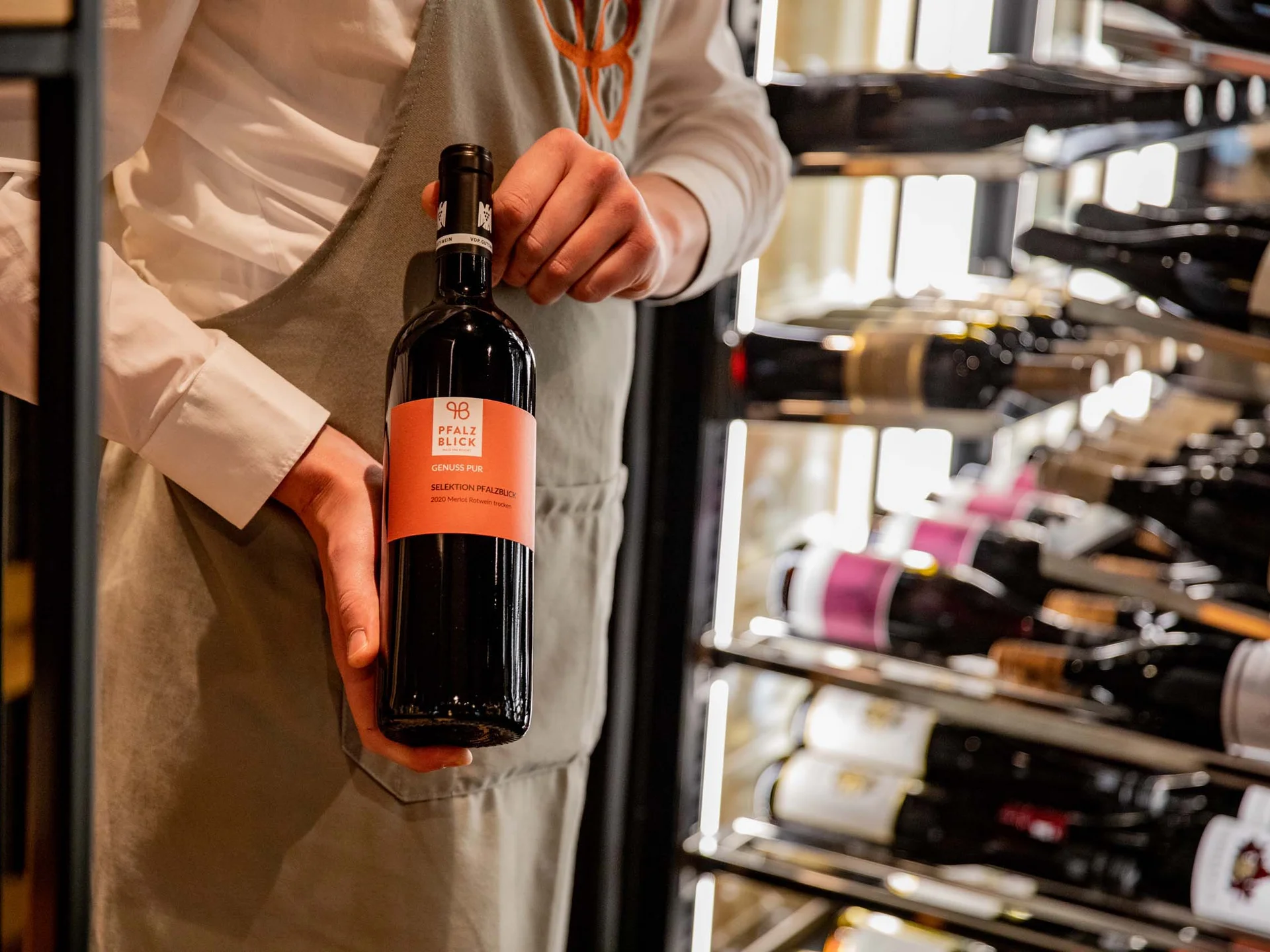 Person hält eine Flasche Rotwein vor einem Weinregal