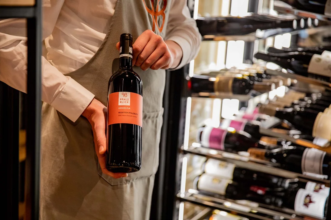 Person hält eine Flasche Rotwein vor einem Weinregal