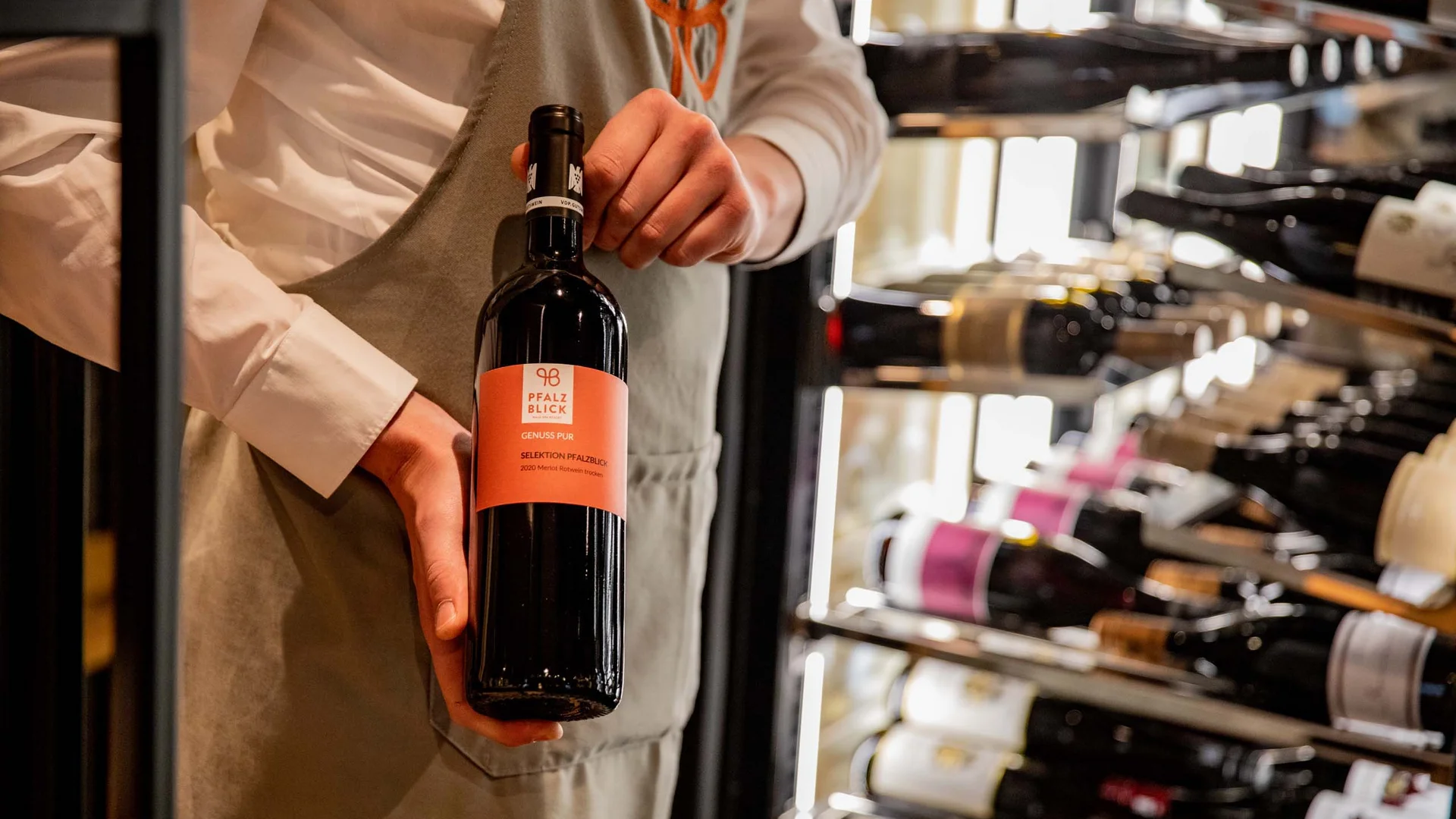 Person hält eine Flasche Rotwein vor einem Weinregal