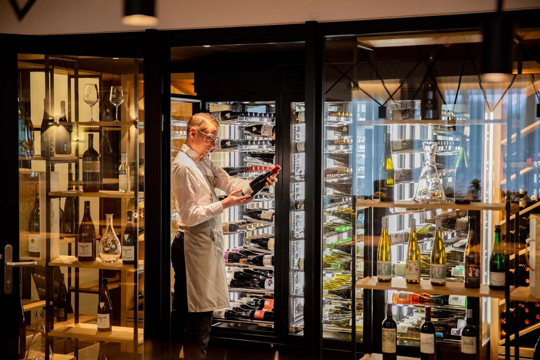 Mann in Schürze wählt Weinflasche aus Weinschrank in einem modernen Raum