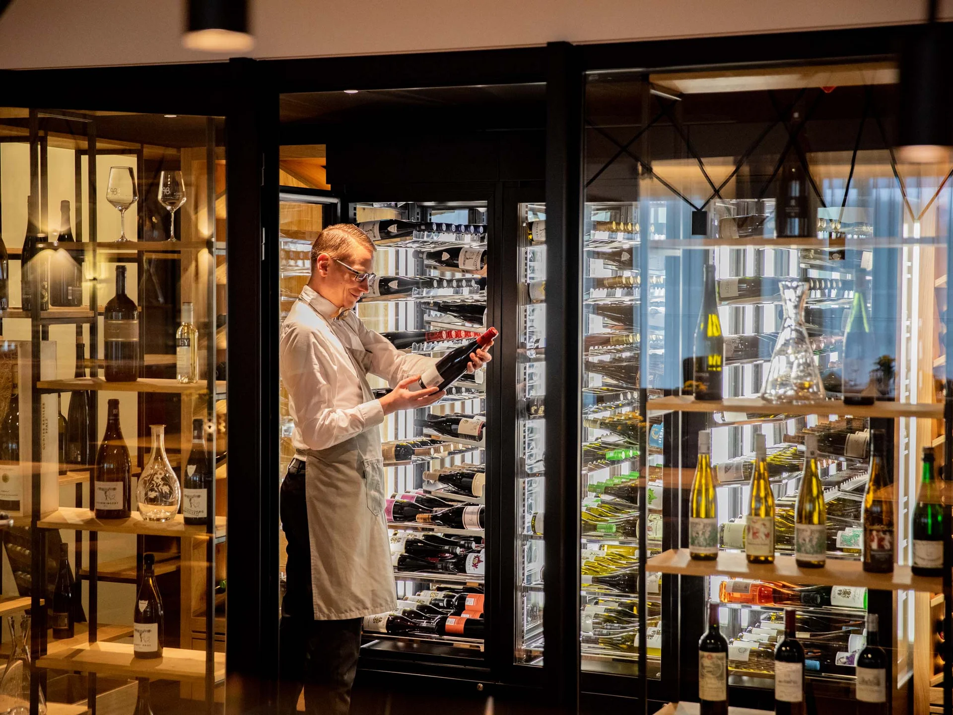 Mann in Schürze wählt Weinflasche aus Weinschrank in einem modernen Raum