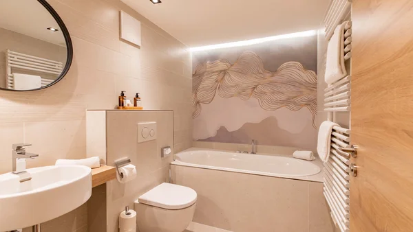 Helles Badezimmer mit Badewanne, Toilette und rundem Spiegel