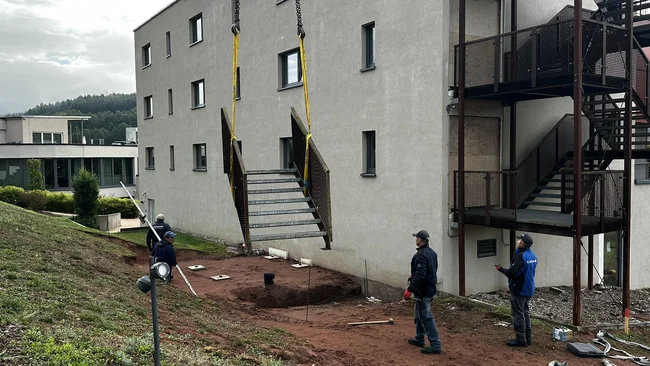 Des ouvriers installent une volée d’escalier extérieur contre un bâtiment