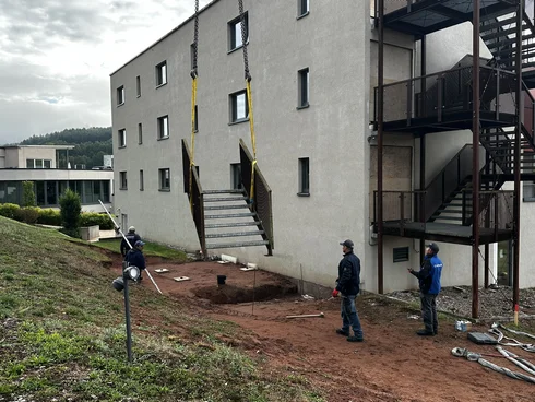 Des ouvriers installent une volée d’escalier extérieur contre un bâtiment