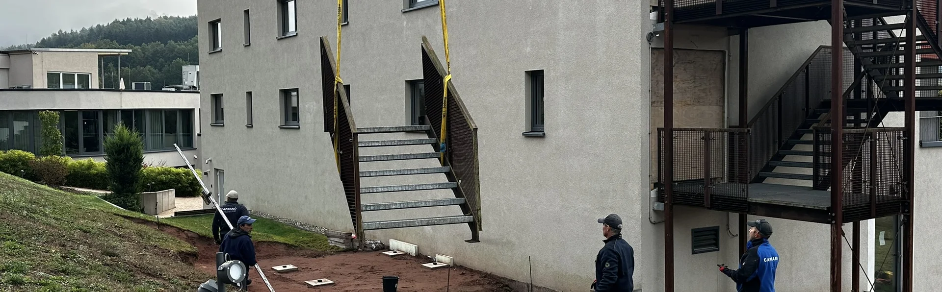 Des ouvriers installent une volée d’escalier extérieur contre un bâtiment
