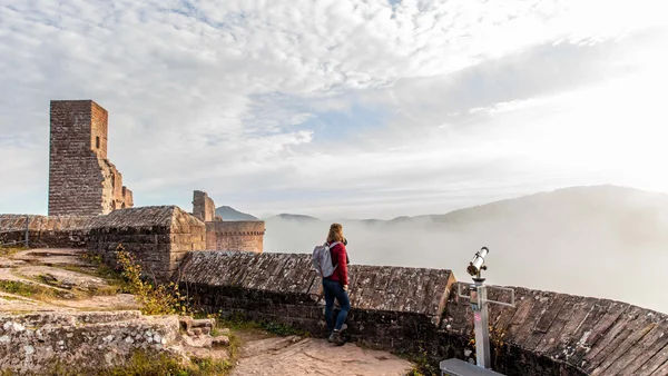 Person mit Rucksack blickt von einer Burgmauer in neblige Berge