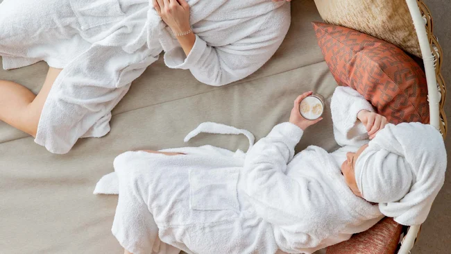Zwei Frauen in Bademänteln entspannen auf einem runden Tagesbett mit Getränken