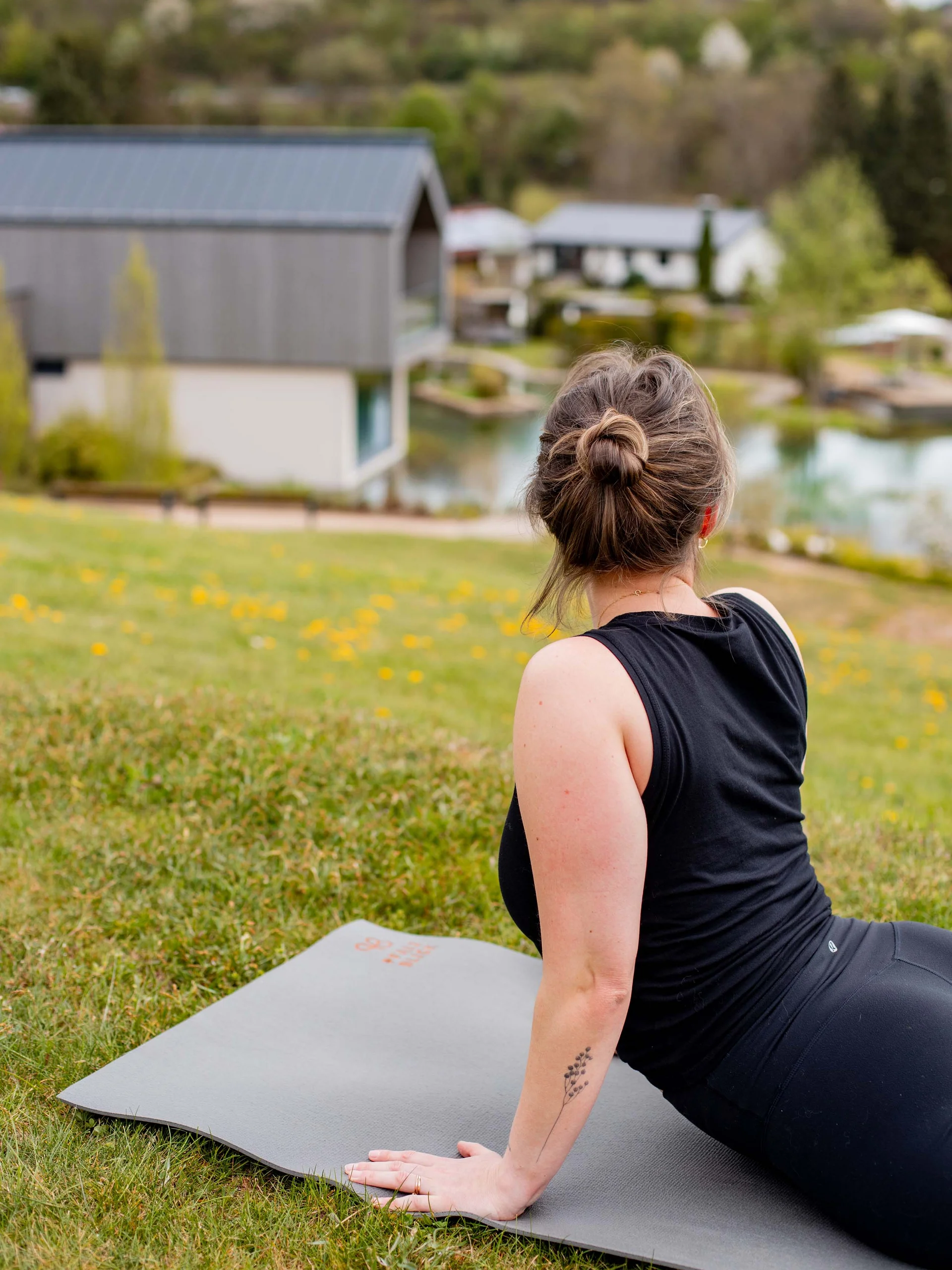 Frau macht Yogaübung auf Matte im Freien mit See und Häusern im Hintergrund