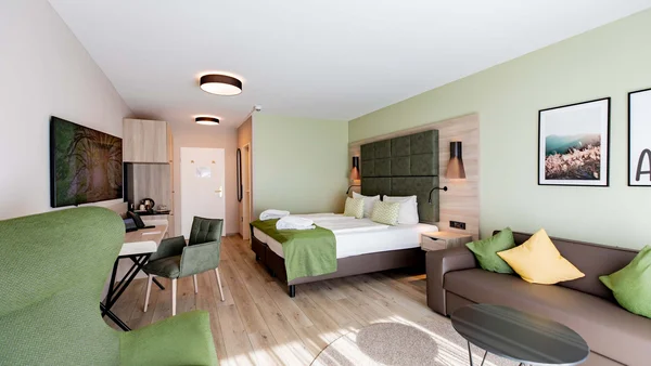 Modernes Hotelzimmer mit Doppelbett, Sofa und grünem Sessel